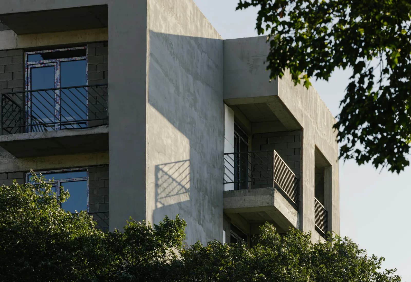 Real estate ad: concrete facade with balconies behind trees