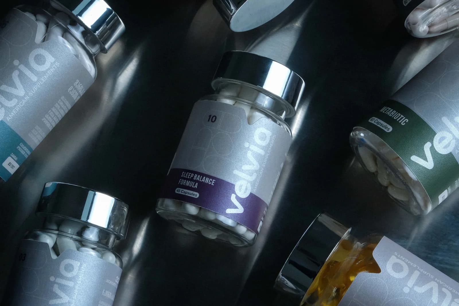 Velvia capsule bottles lying on brushed steel, the Sleep Balance Formula in the centre